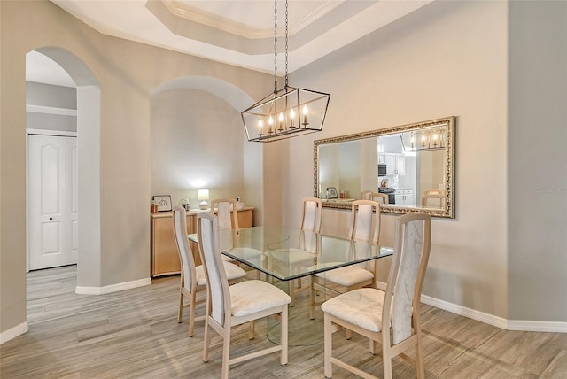 dining area featuring a raised ceiling, ornamental molding, and light wood-type flooring