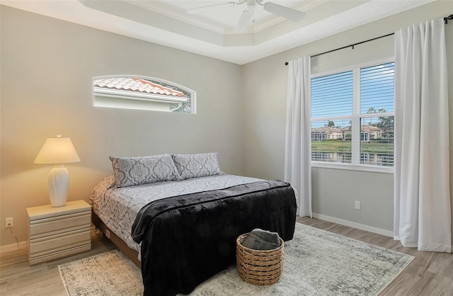 bedroom with a raised ceiling, multiple windows, ceiling fan, and light hardwood / wood-style flooring