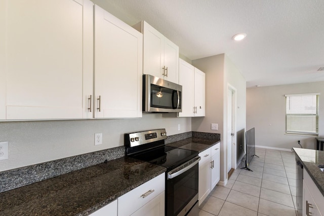 kitchen featuring white cabinets, appliances with stainless steel finishes, dark stone counters, and light tile patterned flooring