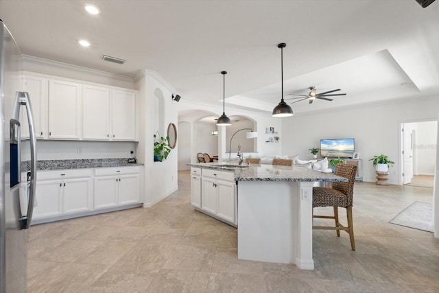 kitchen with white cabinets, decorative light fixtures, stainless steel fridge, and an island with sink