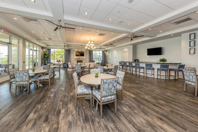 dining space with ceiling fan with notable chandelier, a large fireplace, dark hardwood / wood-style flooring, and coffered ceiling