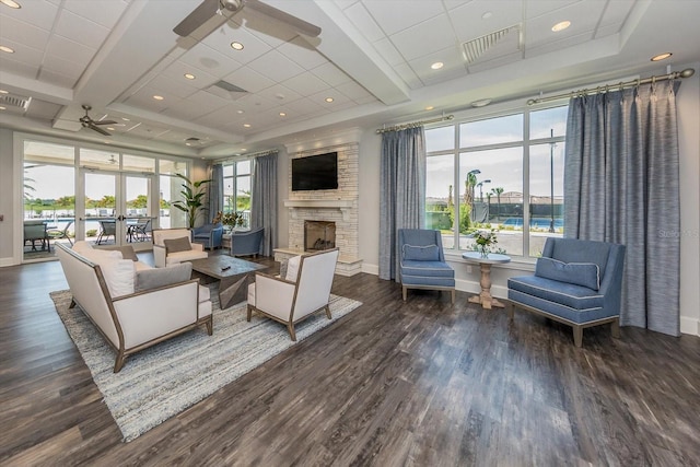 living room featuring dark hardwood / wood-style floors, a stone fireplace, and ceiling fan