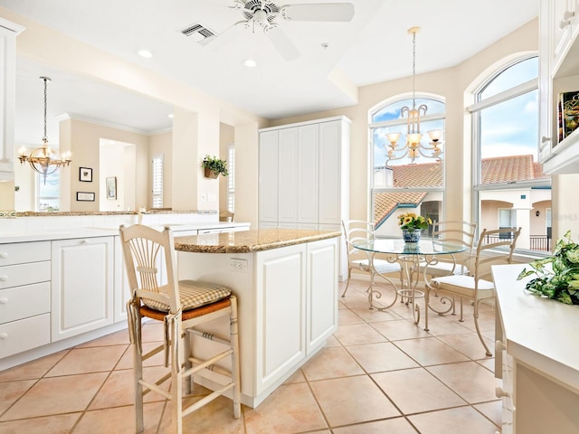 kitchen with white cabinetry, light stone counters, pendant lighting, light tile patterned floors, and ceiling fan with notable chandelier