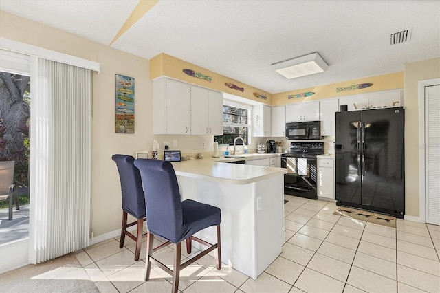 kitchen featuring kitchen peninsula, light tile patterned floors, white cabinetry, and black appliances