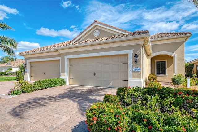 mediterranean / spanish-style home featuring a garage, decorative driveway, a tile roof, and stucco siding