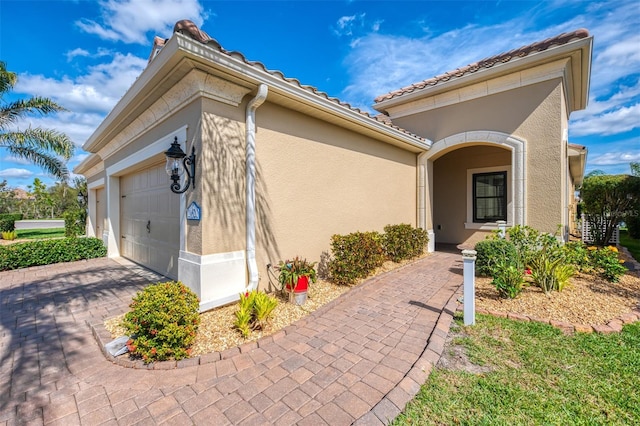 entrance to property featuring decorative driveway, an attached garage, a tile roof, and stucco siding