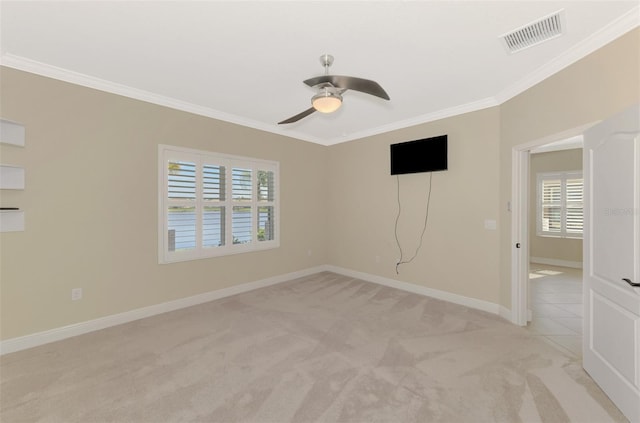 spare room with baseboards, visible vents, light colored carpet, ceiling fan, and crown molding