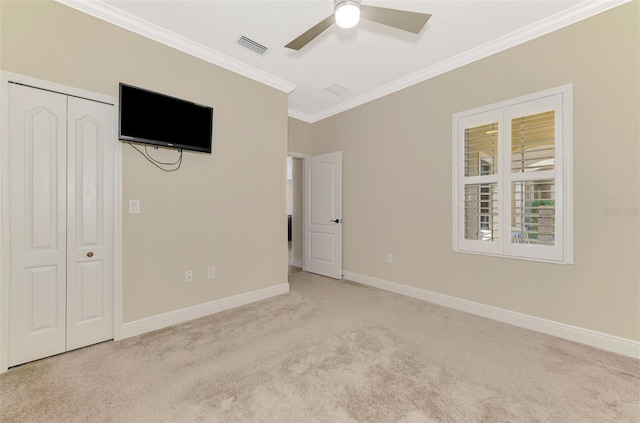 unfurnished bedroom with light carpet, baseboards, a ceiling fan, crown molding, and a closet