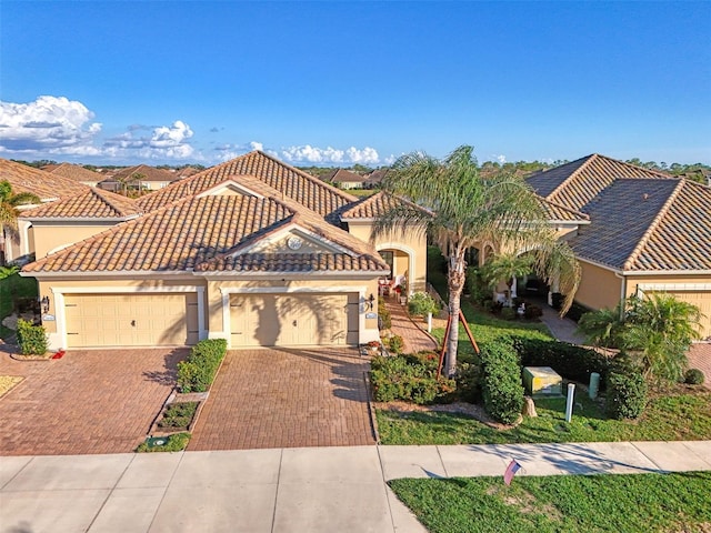 mediterranean / spanish-style home featuring decorative driveway, an attached garage, a tile roof, and stucco siding