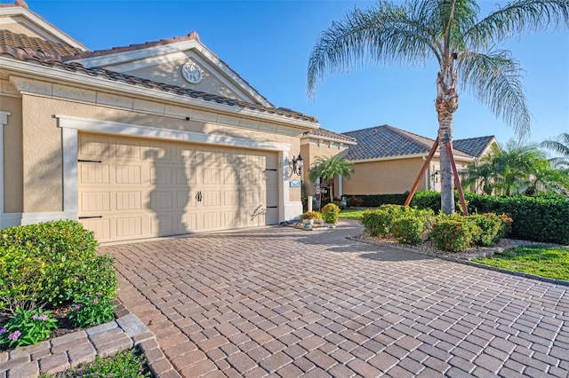 view of front of home featuring a garage, a tiled roof, decorative driveway, and stucco siding