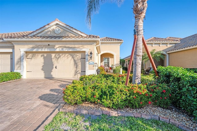 view of front of house featuring a garage, decorative driveway, a tile roof, and stucco siding