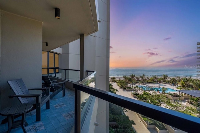 balcony at dusk featuring a water view and a view of the beach