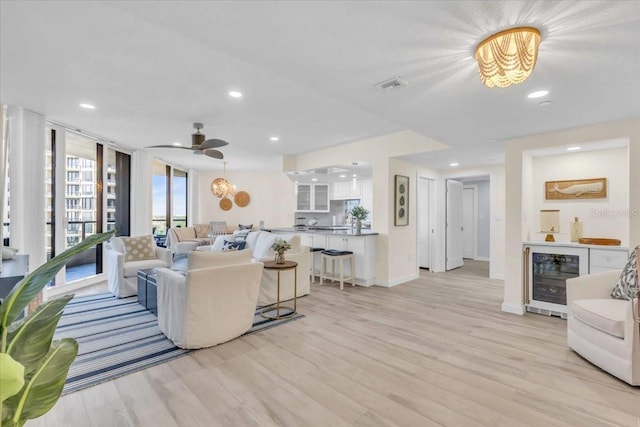 living room featuring ceiling fan, beverage cooler, expansive windows, bar area, and light wood-type flooring