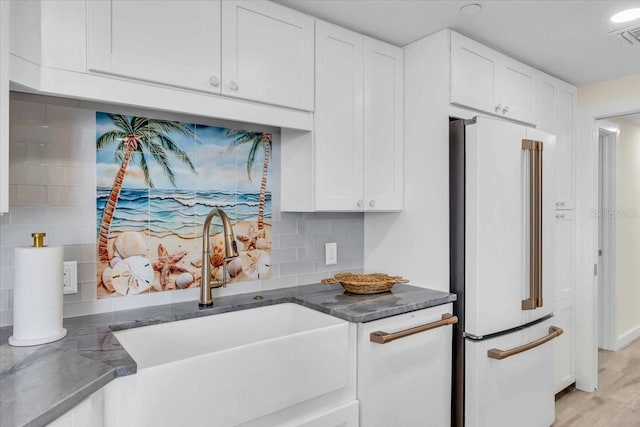 kitchen with backsplash, high end fridge, white cabinets, and sink