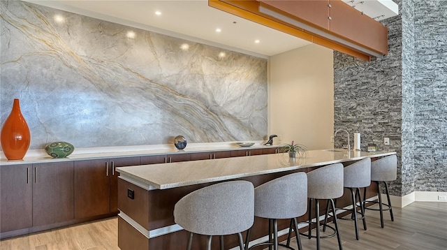 bar with light stone countertops, dark brown cabinets, and light hardwood / wood-style floors