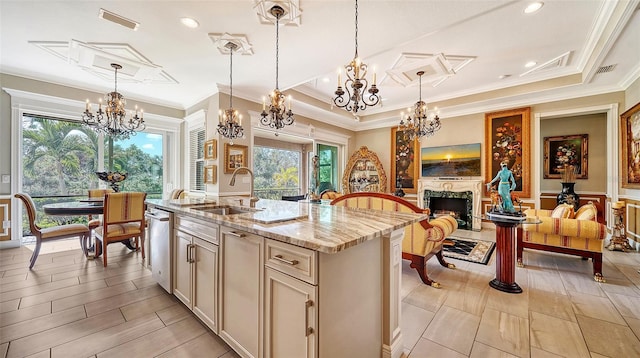 kitchen with a center island with sink, a raised ceiling, sink, light stone countertops, and decorative light fixtures