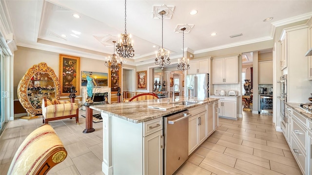 kitchen with pendant lighting, a raised ceiling, sink, an island with sink, and light stone counters