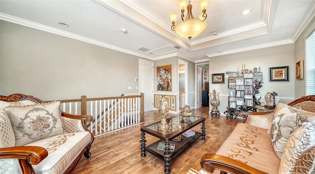 living room featuring hardwood / wood-style flooring, a raised ceiling, ornamental molding, and a notable chandelier