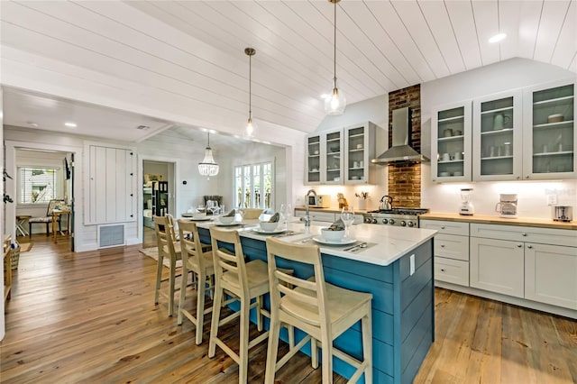 kitchen featuring decorative light fixtures, plenty of natural light, wall chimney exhaust hood, and an island with sink