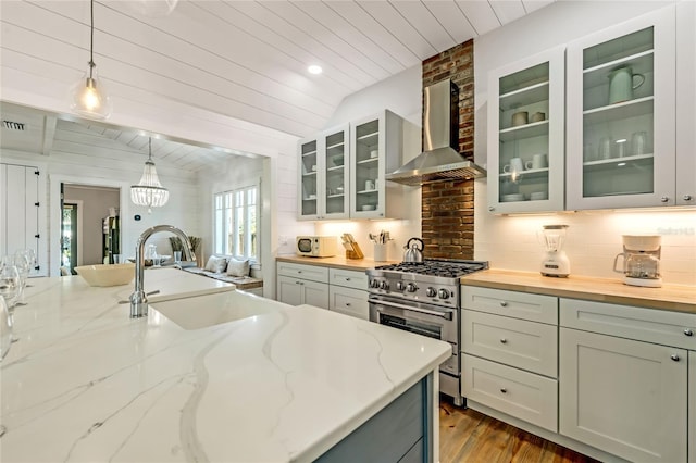 kitchen featuring high end range, wall chimney exhaust hood, sink, pendant lighting, and lofted ceiling