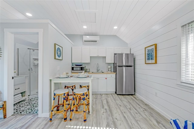 kitchen with a wall mounted AC, sink, light hardwood / wood-style floors, white cabinetry, and stainless steel refrigerator