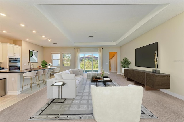 carpeted living room featuring a tray ceiling and sink