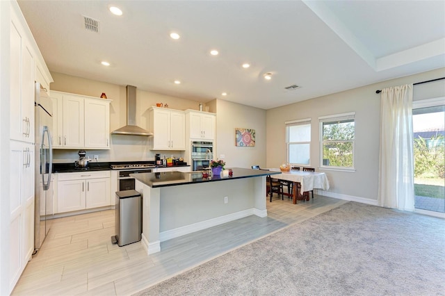 kitchen with a center island with sink, wall chimney exhaust hood, white cabinetry, and appliances with stainless steel finishes