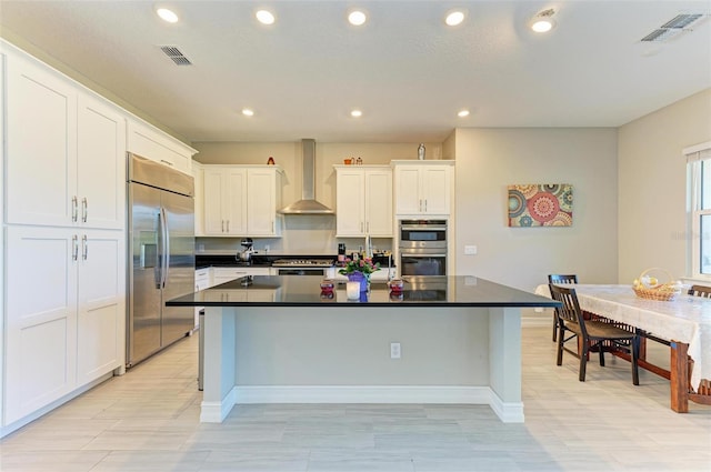 kitchen featuring white cabinetry, wall chimney exhaust hood, stainless steel appliances, a kitchen breakfast bar, and a kitchen island