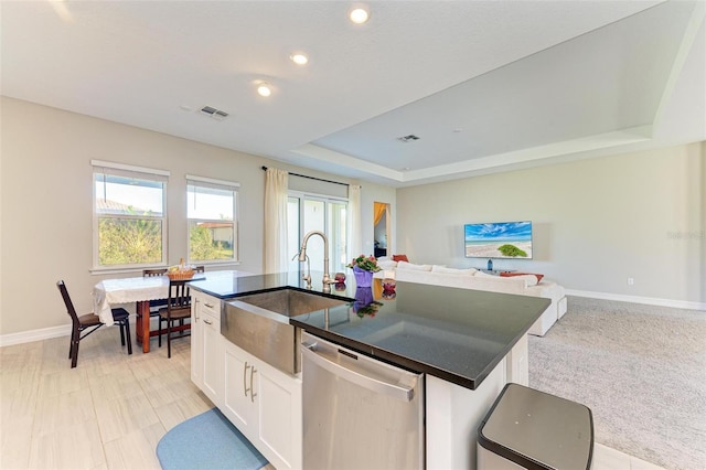 kitchen featuring a center island with sink, sink, stainless steel dishwasher, a tray ceiling, and white cabinetry