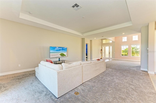 living room featuring a tray ceiling, light carpet, and french doors