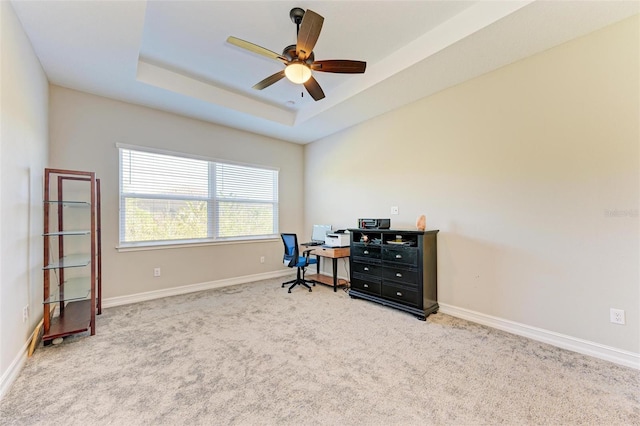 carpeted home office with a raised ceiling and ceiling fan