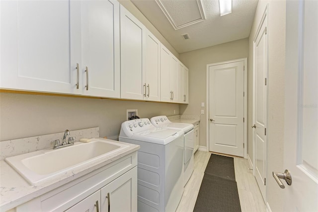 laundry area featuring washing machine and clothes dryer, sink, cabinets, and a textured ceiling