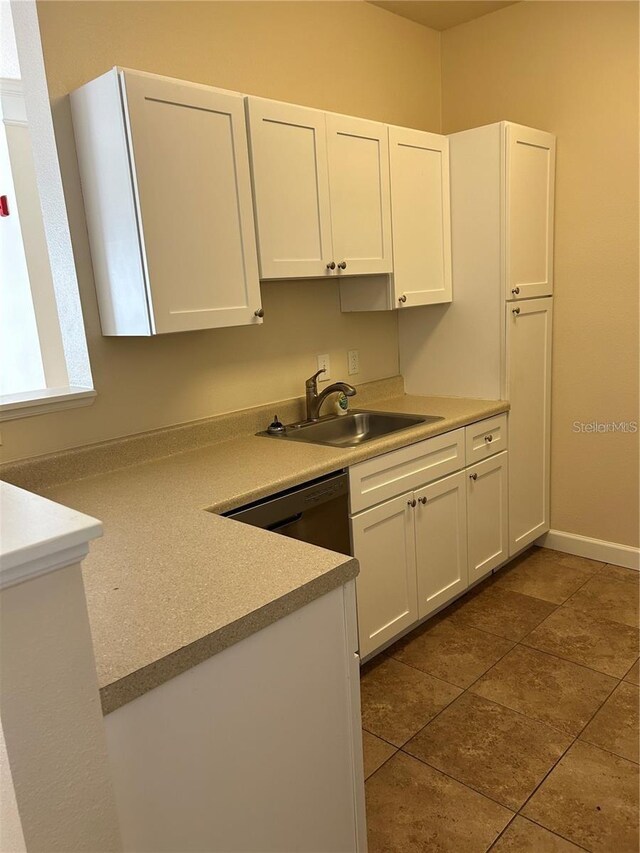 kitchen with dishwashing machine, white cabinetry, dark tile patterned floors, and sink