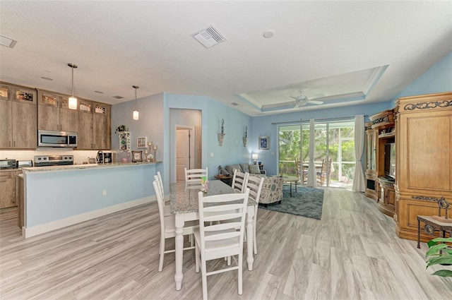 dining room featuring a tray ceiling, ceiling fan, and light hardwood / wood-style floors