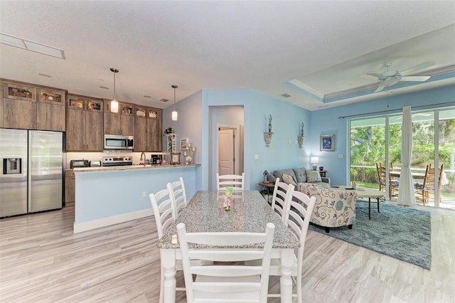 dining area featuring ceiling fan, light hardwood / wood-style floors, a raised ceiling, and a textured ceiling