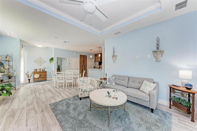 living room with ceiling fan, light hardwood / wood-style floors, crown molding, and a tray ceiling