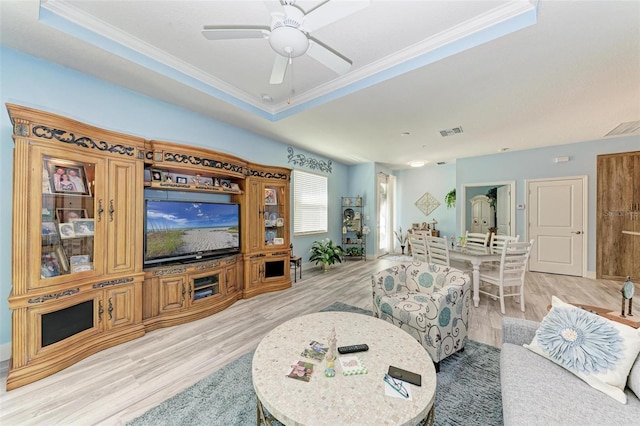 living room with ceiling fan, light hardwood / wood-style floors, a raised ceiling, and crown molding