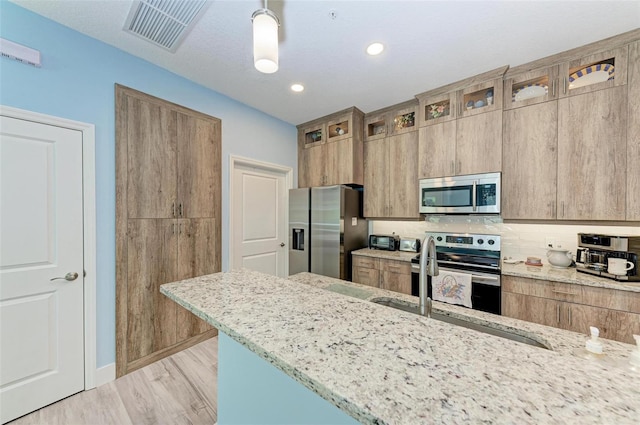 kitchen with light stone countertops, decorative backsplash, stainless steel appliances, sink, and hanging light fixtures