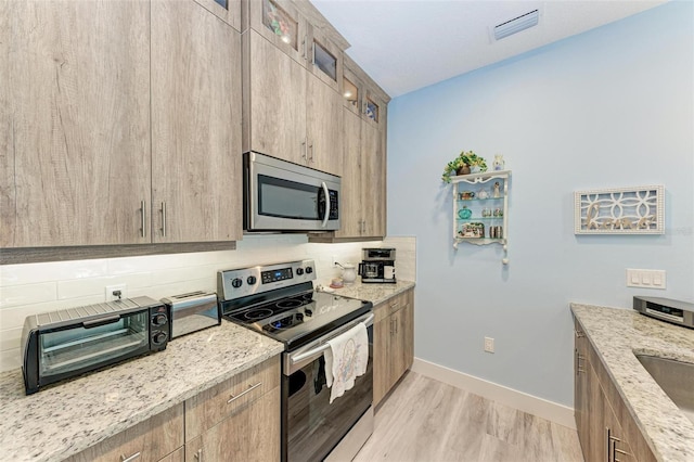 kitchen with decorative backsplash, light stone counters, light hardwood / wood-style floors, and appliances with stainless steel finishes