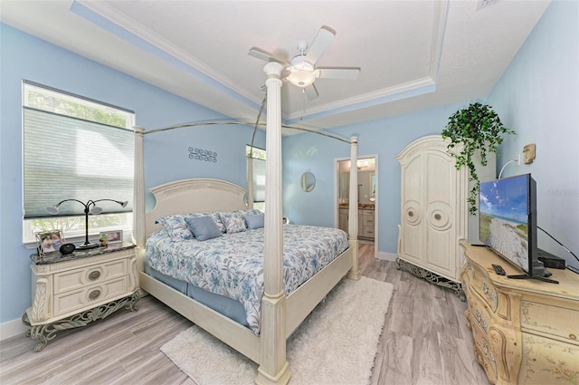 bedroom with crown molding, ensuite bath, ceiling fan, a tray ceiling, and light hardwood / wood-style floors