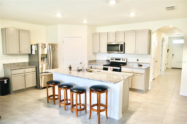 kitchen with appliances with stainless steel finishes, light stone counters, sink, a center island with sink, and a breakfast bar area