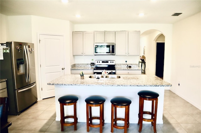 kitchen with appliances with stainless steel finishes, gray cabinetry, and an island with sink