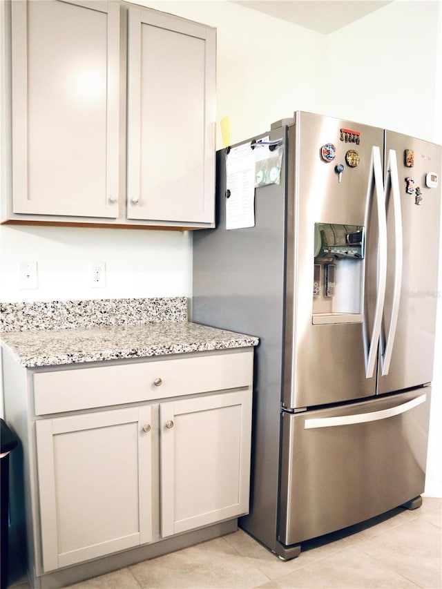 kitchen with light stone countertops, light tile patterned flooring, and stainless steel refrigerator with ice dispenser