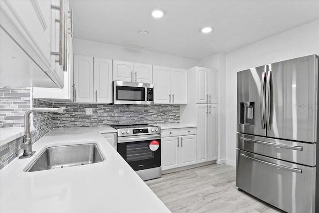 kitchen featuring sink, decorative backsplash, light hardwood / wood-style floors, white cabinetry, and stainless steel appliances