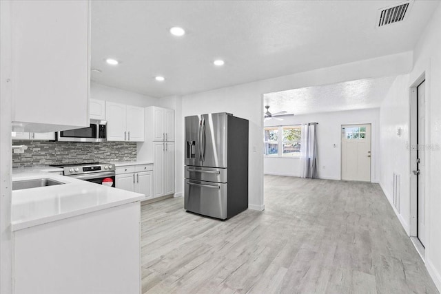 kitchen featuring sink, tasteful backsplash, light hardwood / wood-style floors, white cabinets, and appliances with stainless steel finishes