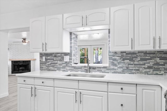 kitchen with backsplash, white cabinets, sink, ceiling fan, and a fireplace