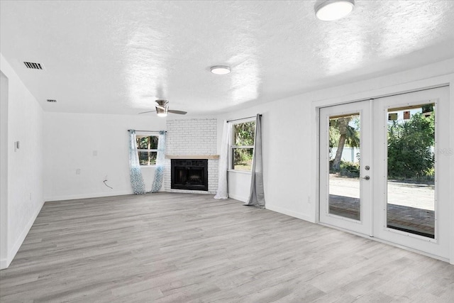 unfurnished living room featuring ceiling fan, french doors, a brick fireplace, a textured ceiling, and light wood-type flooring