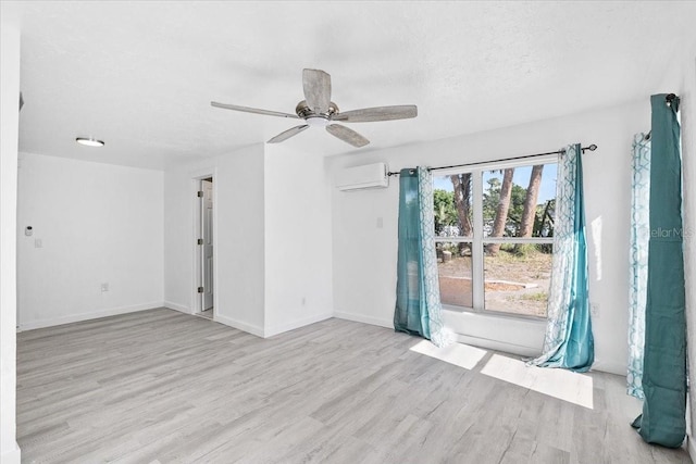 unfurnished room with an AC wall unit, ceiling fan, light hardwood / wood-style floors, and a textured ceiling