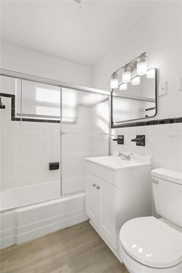 full bathroom featuring hardwood / wood-style flooring, shower / bath combination with glass door, tile walls, vanity, and toilet