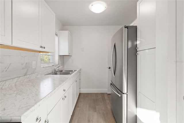 kitchen with sink, light hardwood / wood-style flooring, stainless steel refrigerator, white cabinetry, and decorative backsplash